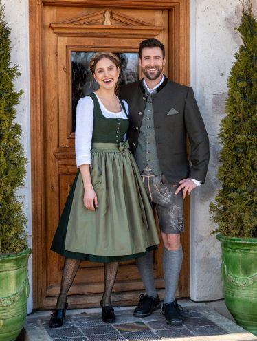 Trachtenpaar - Paarbild Frau mit grünem Dirndl, weißer langarm Bluse und Herr mit grünem Gilet weißes Hemd, bräunliches Sakko und grauer Lederhose (kurz) vor Eingangstür