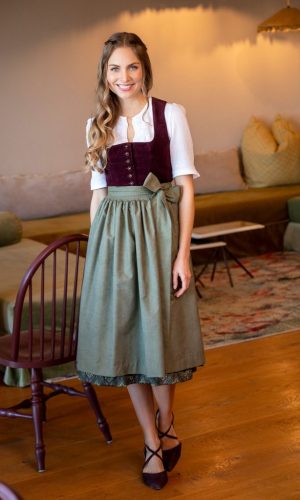 Dame im weinrotem Dirndl mit gemustertem Unterrock und brauner Schürze und weißer Dirndlbluse - halb Arm